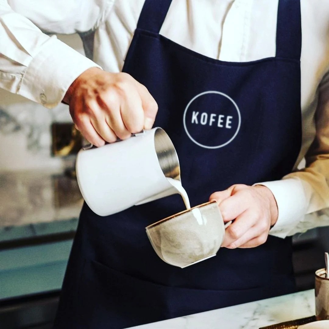A Kofee barista pouring steamed milk into a cup